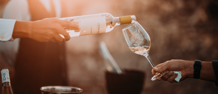 A server serving a glass of white wine.