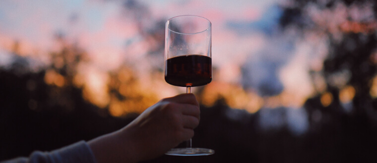 Trees at sunset with a person holding up a glass of red wine.