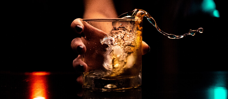 A woman with black painted nails holding a glass of brown liquor.